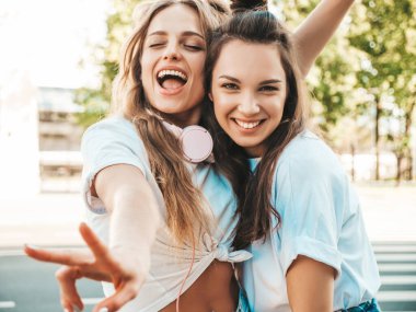 Son moda beyaz tişörtlü iki güzel gülümseyen hippi kadın portresi. Sokakta poz veren kaygısız kadınlar. Pozitif modeller eğleniyor, sarılıyor ve deliriyor.