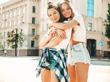 Son moda beyaz tişörtlü iki güzel gülümseyen hippi kadın portresi. Sokakta poz veren kaygısız kadınlar. Pozitif modeller eğleniyor, sarılıyor ve deliriyor.