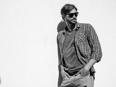 Yakışıklı, şık, gülümseyen hipster Lambersex modelinin portresi. Kareli gömlek giymiş bir adam. Moda erkek, güneş gözlüklü beyaz duvarın yanında poz veriyor. Siyah ve beyaz