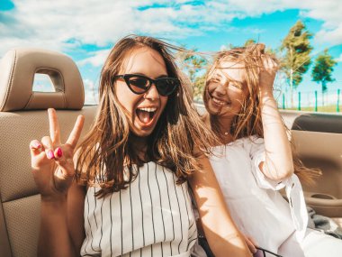 Üstü açık arabadaki iki güzel ve gülümseyen hippi kadının portresi. Cabriolet kullanan kaygısız seksi kadınlar. Pozitif modeller dışarıda güneş gözlüğü takıp eğleniyorlar. Yaz günlerinin tadını çıkarıyorlar.