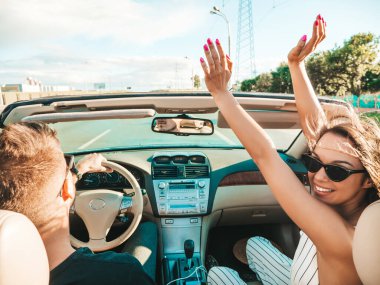 Genç, güzel, gülümseyen hippi kadın ve üstü açık arabadaki erkek arkadaşının portresi. Cabriolet kullanan kaygısız seksi kadın. Pozitif model sürme ve güneş gözlükleriyle eğlenme. Yaz günlerinin tadını çıkarıyorum.
