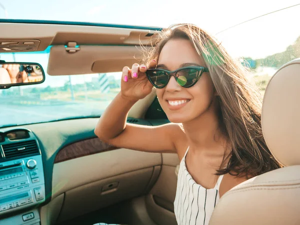 Üstü açık arabadaki güzel ve gülümseyen yeniyetme kadın portresi. Cabriolet kullanan kaygısız seksi kadın. Pozitif model sürüş ve gün batımında güneş gözlüğüyle eğlenme. Keyifli yaz günleri