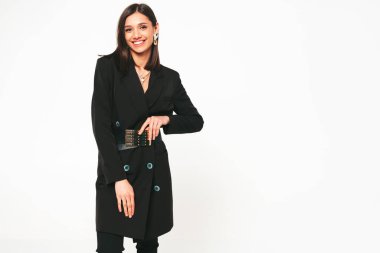 Güzel, güler yüzlü, güzel, siyah iş elbisesi içinde esmer bir kadın. Stüdyoda gri arka planda poz veren kaygısız bir kadın. Parlak akşam makyajlı, şık bir model.