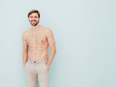 Yakışıklı, güçlü bir adamın portresi. Sağlıklı gülümseyen atletik spor modelinin açık mavi duvarın yanında poz vermesi. Çıplak gövdesi olan kendine güvenen seksi moda erkeği. Lambersexual stüdyoda.