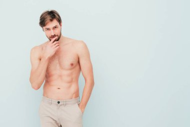 Yakışıklı, güçlü bir adamın portresi. Sağlıklı gülümseyen atletik spor modelinin açık mavi duvarın yanında poz vermesi. Çıplak gövdesi olan kendine güvenen seksi moda erkeği. Lambersexual stüdyoda.