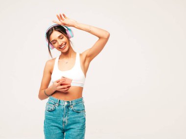 Kot pantolon giymiş, gülümseyen güzel bir kadın. Kablosuz kulaklıkla müzik dinleyen seksi tasasız model. Stüdyoda gri arka planda poz veren sevimli ve pozitif bir kadın. Akıllı telefon tutuluyor