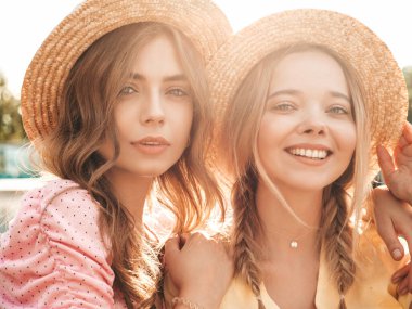 İki genç, güzel, gülümseyen yeniyetme kadın, modaya uygun bir yaz elbisesi içinde. Sokakta şapkalarla poz veren kaygısız seksi kadınlar. Sunset 'te olumlu modeller var. Çiçek tutuyorlar.