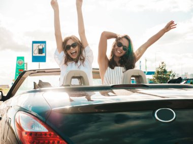 Üstü açık arabadaki iki güzel ve gülümseyen hippi kadının portresi. Cabriolet kullanan kaygısız seksi kadınlar. Pozitif modeller dışarıda güneş gözlüğü takıp eğleniyorlar. Yaz günlerinin tadını çıkarıyorlar.