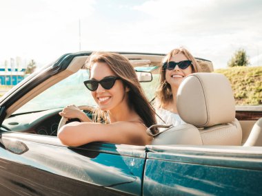 Üstü açık arabadaki iki güzel ve gülümseyen hippi kadının portresi. Cabriolet kullanan kaygısız seksi kadınlar. Pozitif modeller dışarıda güneş gözlüğü takıp eğleniyorlar. Yaz günlerinin tadını çıkarıyorlar.