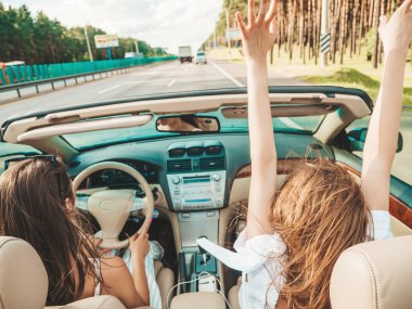 Üstü açık arabadaki iki güzel ve gülümseyen hippi kadının portresi. Cabriolet kullanan kaygısız seksi kadınlar. Pozitif modeller dışarıda güneş gözlüğü takıp eğleniyorlar. Yaz günlerinin tadını çıkarıyorlar.