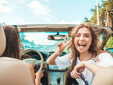 Üstü açık arabadaki iki güzel ve gülümseyen hippi kadının portresi. Cabriolet kullanan kaygısız seksi kadınlar. Pozitif modeller dışarıda güneş gözlüğü takıp eğleniyorlar. Yaz günlerinin tadını çıkarıyorlar.