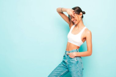 Beyaz formalı bluz ve kot pantolon giymiş güzel bir kadın. Seksi kaygısız neşeli model sabahının tadını çıkarıyor. Stüdyoda mavi duvarın yanında poz veren sevimli ve pozitif bir kadın.