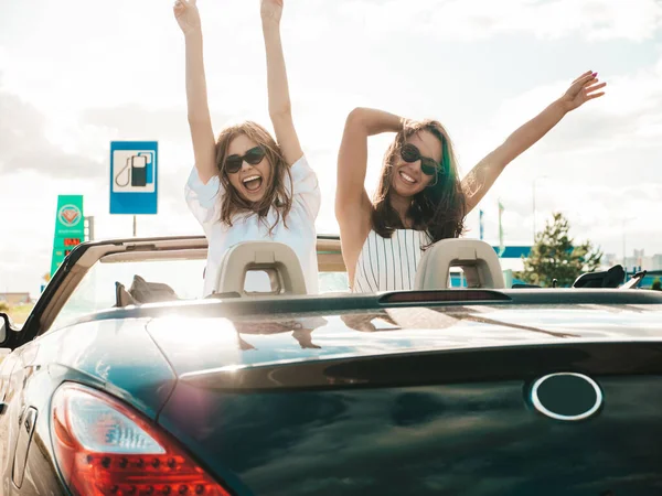 Üstü açık arabadaki iki güzel ve gülümseyen hippi kadının portresi. Cabriolet kullanan kaygısız seksi kadınlar. Pozitif modeller dışarıda güneş gözlüğü takıp eğleniyorlar. Yaz günlerinin tadını çıkarıyorlar.