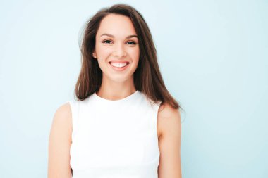 Moda dolu beyaz tişörtlü, gülümseyen genç bir kadının yakın plan portresi. Stüdyoda açık mavi duvarın yanında poz veren kaygısız seksi kadın. Pozitif model içeride eğleniyor. Neşeli ve mutlu