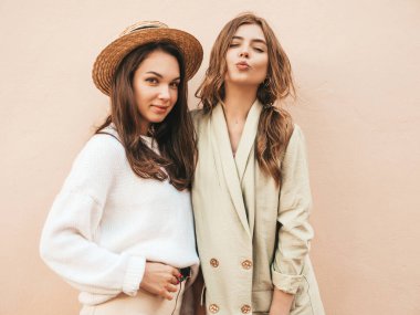 Son moda beyaz süveter ve palto giymiş iki güzel, gülümseyen hippi kadın. Sokakta şapkayla poz veren seksi kaygısız kadınlar. Pozitif modeller eğleniyor. Açık havada iletişim kurmak. 