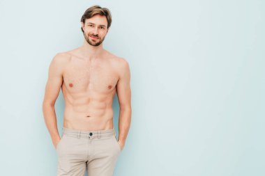 Yakışıklı, güçlü bir adamın portresi. Sağlıklı gülümseyen atletik spor modelinin açık mavi duvarın yanında poz vermesi. Çıplak gövdesi olan kendine güvenen seksi moda erkeği. Lambersexual stüdyoda.