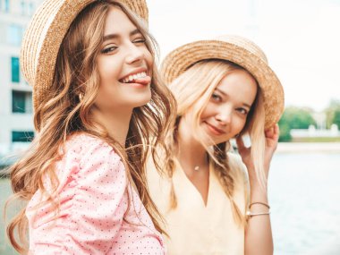 İki genç, güzel, gülümseyen yeniyetme kadın, modaya uygun bir yaz elbisesi içinde. Sokakta şapkalarla poz veren kaygısız seksi kadınlar. Sunset 'te pozitif modeller