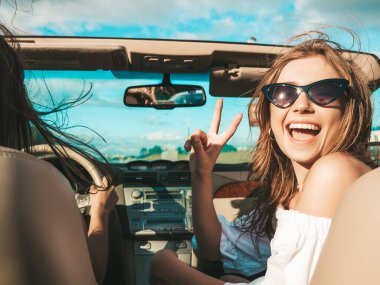 Üstü açık arabadaki iki güzel ve gülümseyen hippi kadının portresi. Cabriolet kullanan kaygısız seksi kadınlar. Pozitif modeller dışarıda güneş gözlüğü takıp eğleniyorlar. Yaz günlerinin tadını çıkarıyorlar.