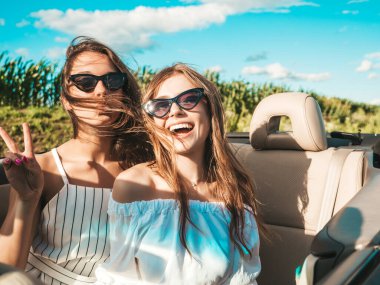 Üstü açık arabadaki iki güzel ve gülümseyen hippi kadının portresi. Cabriolet kullanan kaygısız seksi kadınlar. Pozitif modeller dışarıda güneş gözlüğü takıp eğleniyorlar. Yaz günlerinin tadını çıkarıyorlar.