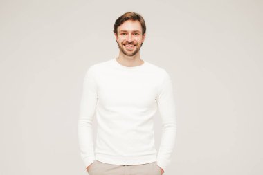 Beyaz süveter ve pantolon giyen yakışıklı, gülümseyen hippi, keresteci iş adamı modeli portresi. Stüdyoda gri arka planda poz veren modacı.