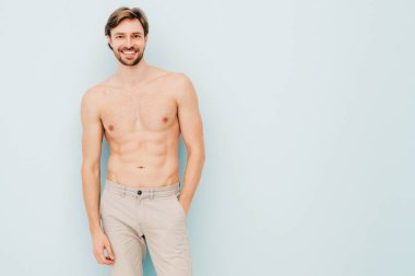 Yakışıklı, güçlü bir adamın portresi. Sağlıklı gülümseyen atletik spor modelinin açık mavi duvarın yanında poz vermesi. Çıplak gövdesi olan kendine güvenen seksi moda erkeği. Lambersexual stüdyoda.