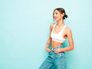 Beyaz formalı bluz ve kot pantolon giymiş güzel bir kadın. Seksi kaygısız neşeli model sabahının tadını çıkarıyor. Stüdyoda mavi duvarın yanında poz veren sevimli ve pozitif bir kadın.