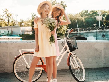İki genç, güzel, gülümseyen yeniyetme kadın, modaya uygun bir yaz elbisesi içinde. Sokakta şapkalarla poz veren kaygısız seksi kadınlar. Gün batımında bisiklet yakınlarında pozitif modeller. 