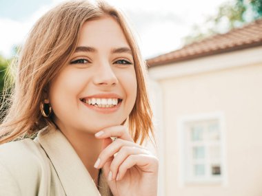 Güzel, gülümseyen sarışın modelin yakın plan portresi. Sokakta poz veren modaya uygun bir kadın. Komik ve pozitif bir kadın gün batımında dışarıda eğleniyor. Güzel ve neşeli.