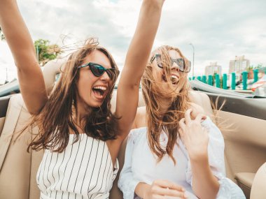 Üstü açık arabadaki iki güzel ve gülümseyen hippi kadının portresi. Cabriolet kullanan kaygısız seksi kadınlar. Pozitif modeller dışarıda güneş gözlüğü takıp eğleniyorlar. Yaz günlerinin tadını çıkarıyorlar.