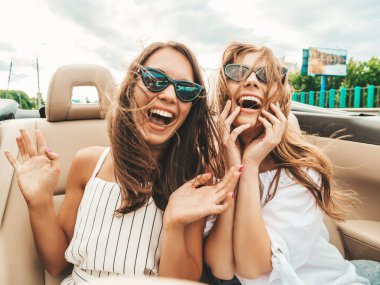 Üstü açık arabadaki iki güzel ve gülümseyen hippi kadının portresi. Cabriolet kullanan kaygısız seksi kadınlar. Pozitif modeller dışarıda güneş gözlüğü takıp eğleniyorlar. Yaz günlerinin tadını çıkarıyorlar.