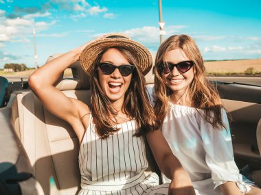 Üstü açık arabadaki iki güzel ve gülümseyen hippi kadının portresi. Cabriolet kullanan kaygısız seksi kadınlar. Pozitif modeller dışarıda güneş gözlüğü takıp eğleniyorlar. Yaz günlerinin tadını çıkarıyorlar.