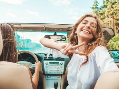 Üstü açık arabadaki iki güzel ve gülümseyen hippi kadının portresi. Cabriolet kullanan kaygısız seksi kadınlar. Pozitif modeller dışarıda güneş gözlüğü takıp eğleniyorlar. Yaz günlerinin tadını çıkarıyorlar.