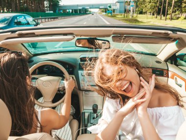 Üstü açık arabadaki iki güzel ve gülümseyen hippi kadının portresi. Cabriolet kullanan kaygısız seksi kadınlar. Pozitif modeller dışarıda güneş gözlüğü takıp eğleniyorlar. Yaz günlerinin tadını çıkarıyorlar.