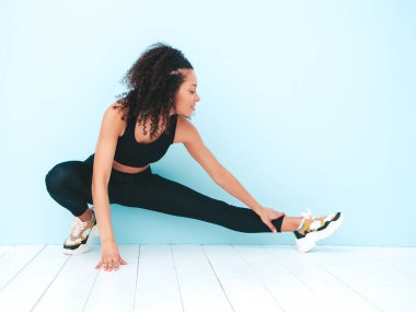 Spor kıyafetleriyle gülümseyen siyah kadın portresi, afro kıvırcık saç stili. Spor giysisi giyiyor. Eğitimden önce esneyen genç ve güzel bir model.