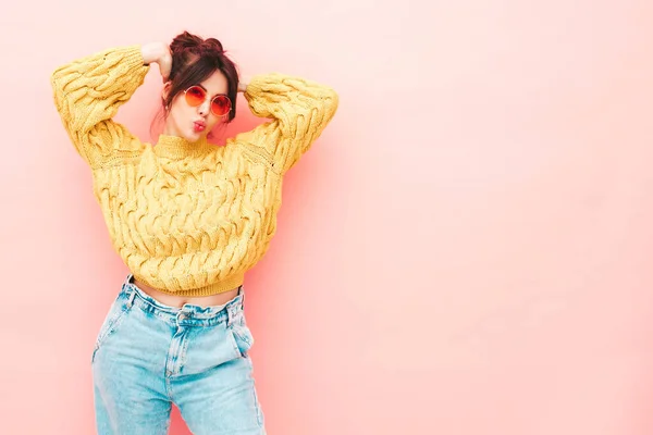 流行の夏の黄色のヒップスターセーターとジーンズの若い美しい笑顔の女性 スタジオでピンク色の壁の近くにポーズをとるセクシーな屈託のない女性 サングラスで楽しい正のモデル — ストック写真
