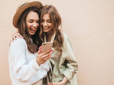 İki güzel, gülümseyen hippi kadın. Sokakta şapkalarla poz veren kaygısız seksi kadınlar. Modeller eğleniyor. Cep telefonu ekranına bakıp gülüyorlar. Mobil uygulamalar kullanarak eğleniyorlar.