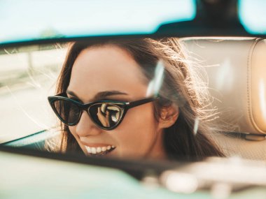 Üstü açık arabadaki güzel ve gülümseyen hippi kız portresi. Cabriolet kullanan kaygısız seksi kadın. Pozitif model sürüş ve güneş gözlükleriyle eğlenme. Dikiz aynasından yansıyor.