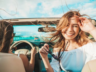 Üstü açık arabadaki iki güzel ve gülümseyen hippi kadının portresi. Cabriolet kullanan kaygısız seksi kadınlar. Pozitif modeller dışarıda güneş gözlüğü takıp eğleniyorlar. Yaz günlerinin tadını çıkarıyorlar.