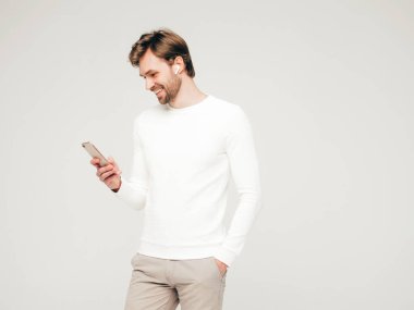 Yakışıklı, güler yüzlü hippi, keresteci iş adamı, beyaz bir süveter ve takım elbise giyiyor. Stüdyoda gri arka planda poz veren modacı tarzı bir adam. Akıllı telefonu elinde tutarak. Kulaklıkla.