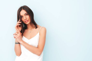 Beyaz pijama giymiş gülümseyen güzel bir kadının portresi. Seksi kaygısız neşeli model sabahının tadını çıkarıyor. Stüdyoda açık mavi duvarın yanında poz veren sevimli ve pozitif bir kadın. Bronzlaşmış ve zayıf