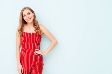 Yeni moda kırmızı takım elbiseli güzel, gülümseyen bir kadının portresi. Stüdyoda açık mavi duvarın yanında poz veren kaygısız seksi kadın. Pozitif model içeride eğleniyor. Neşeli ve mutlu