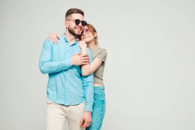 Gülümseyen güzel kadın ve yakışıklı erkek arkadaşı. Mutlu, neşeli bir aile stüdyodaki gri arka planda hassas anlar yaşıyor. Saf, neşeli modeller sarılıyor. Güneş gözlükleriyle birbirlerine sarılıyorlar. 