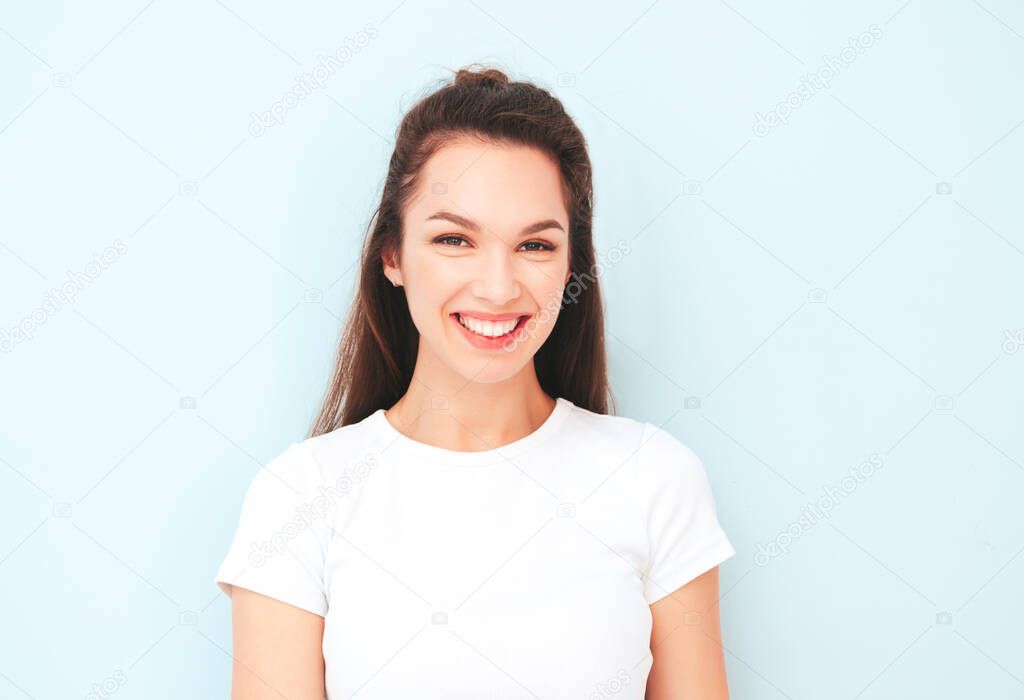 Closeup portrait of young beautiful smiling female in trendy summer hipster clothes. Sexy carefree woman posing near light blue wall in studio. Positive model having fun indoors. Cheerful and happy 
