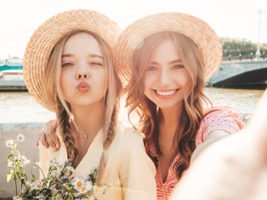 İki genç, güzel, gülümseyen yeniyetme kadın, modaya uygun bir yaz elbisesi içinde. Sokakta şapkalarla poz veren kaygısız seksi kadınlar. Sunset 'te pozitif modeller var. Pov selfie çekiliyor