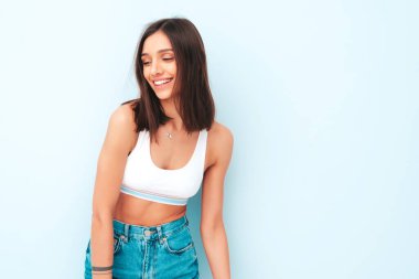 Beyaz formalı bluz ve kot pantolon giymiş güzel bir kadın. Seksi kaygısız neşeli model sabahının tadını çıkarıyor. Şirin ve pozitif kadın stüdyoda açık mavi duvarın yanında poz veriyor.