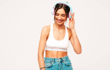 Kot pantolon giymiş, gülümseyen güzel bir kadın. Kablosuz kulaklıkla müzik dinleyen seksi tasasız model. Stüdyoda gri arka planda poz veren sevimli ve pozitif kadın.