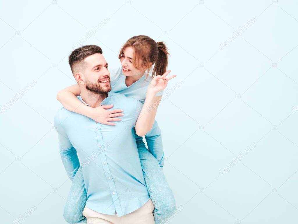Smiling beautiful woman and her handsome boyfriend.Happy cheerful family having tender moments near light blue wall in studio.Pure models hugging.Embracing each other.Male gives piggyback riding