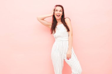 Modayı takip eden yaz hippi kıyafetleri içinde gülümseyen güzel bir kadının portresi. Stüdyoda pembe duvarın yanında poz veren kaygısız seksi kadın. Kapalı alanda eğlenen pozitif model.