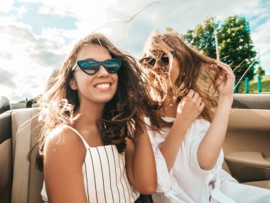 Üstü açık arabadaki iki güzel ve gülümseyen hippi kadının portresi. Cabriolet kullanan kaygısız seksi kadınlar. Pozitif modeller dışarıda güneş gözlüğü takıp eğleniyorlar. Yaz günlerinin tadını çıkarıyorlar.