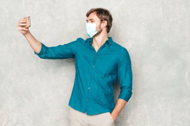 Yakışıklı, güler yüzlü hippi, keresteci iş adamı mankeni, günlük kot gömlek giyiyor. Moda tarzı bir adam stüdyoda gri duvara karşı poz veriyor. Korona virüsü için koruyucu maske takıyor. Selfie çekiyorum. 